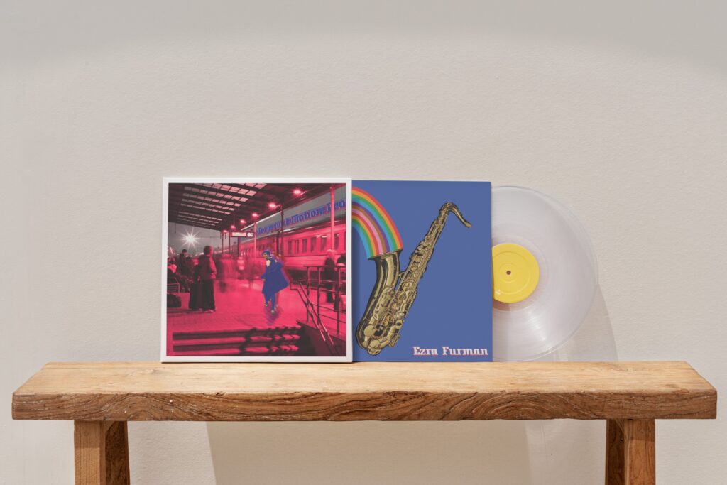photo of a vinyl record with the redesigned cover of "Perpetual Motion People." Ezra Furman runs through a pink tinted train station with the words of the album title, zooming above her above near a train, parked in a station